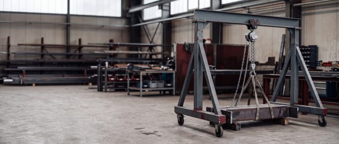 Fahrbarer Portalkran aus Aluminium mit Kettenzug über einem Stahlteil auf dem Werkstattboden