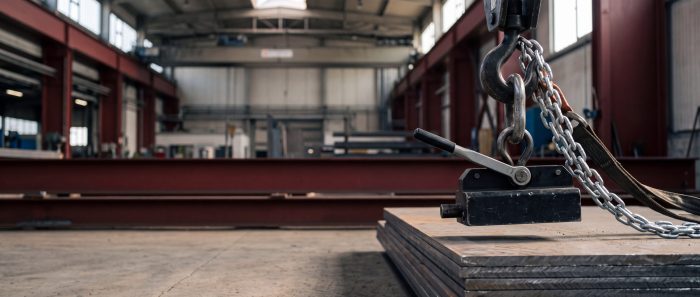 Permanent-Lasthebemagnet mit Schalthebel am Kranhaken über einem Stapel Stahlplatten