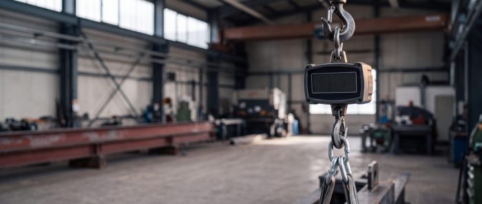 Kranwaage zwischen Kranhaken und Kettengehänge, das ein Stahlteil trägt